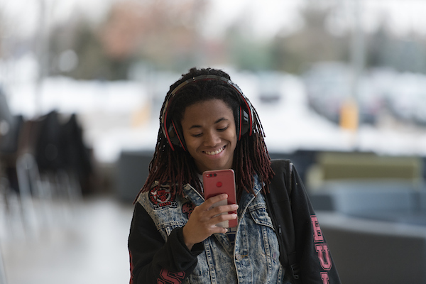 Person smiling at phone while wearing headphones, blurred background.