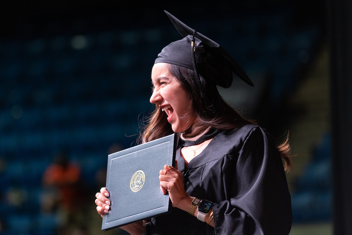 female student smiling at crowd with diploma