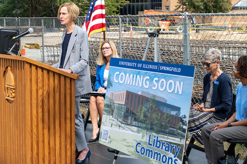 Chancellor give remarks at a podium next to a sign that says Coming Soon, Library Commons