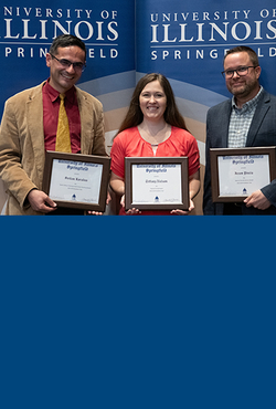 Three faculty members stand holding awards.