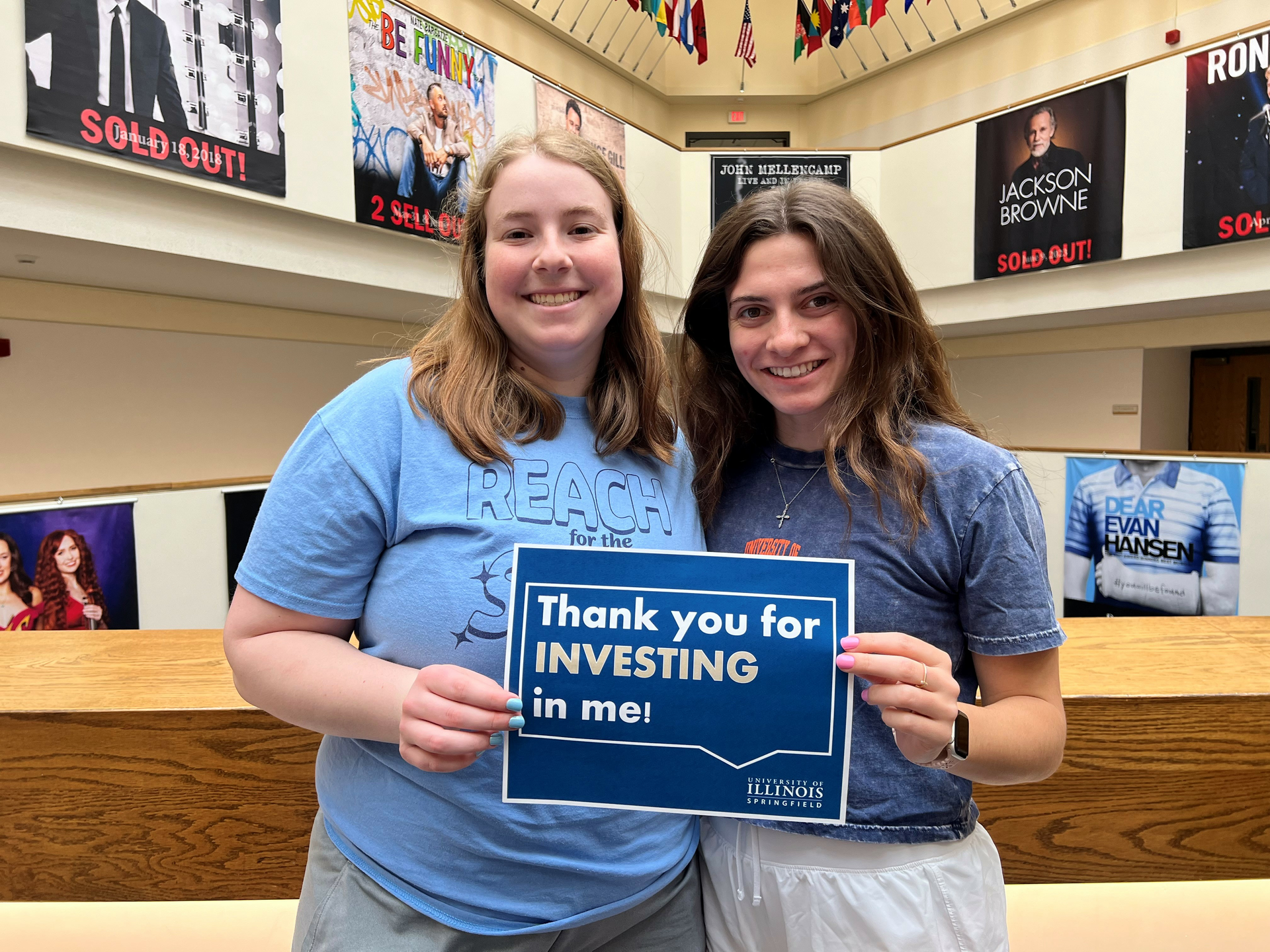 Two female students holding a sign that reads "Thank you for investing in me" with the University of Illinois Springfield wordmark. 