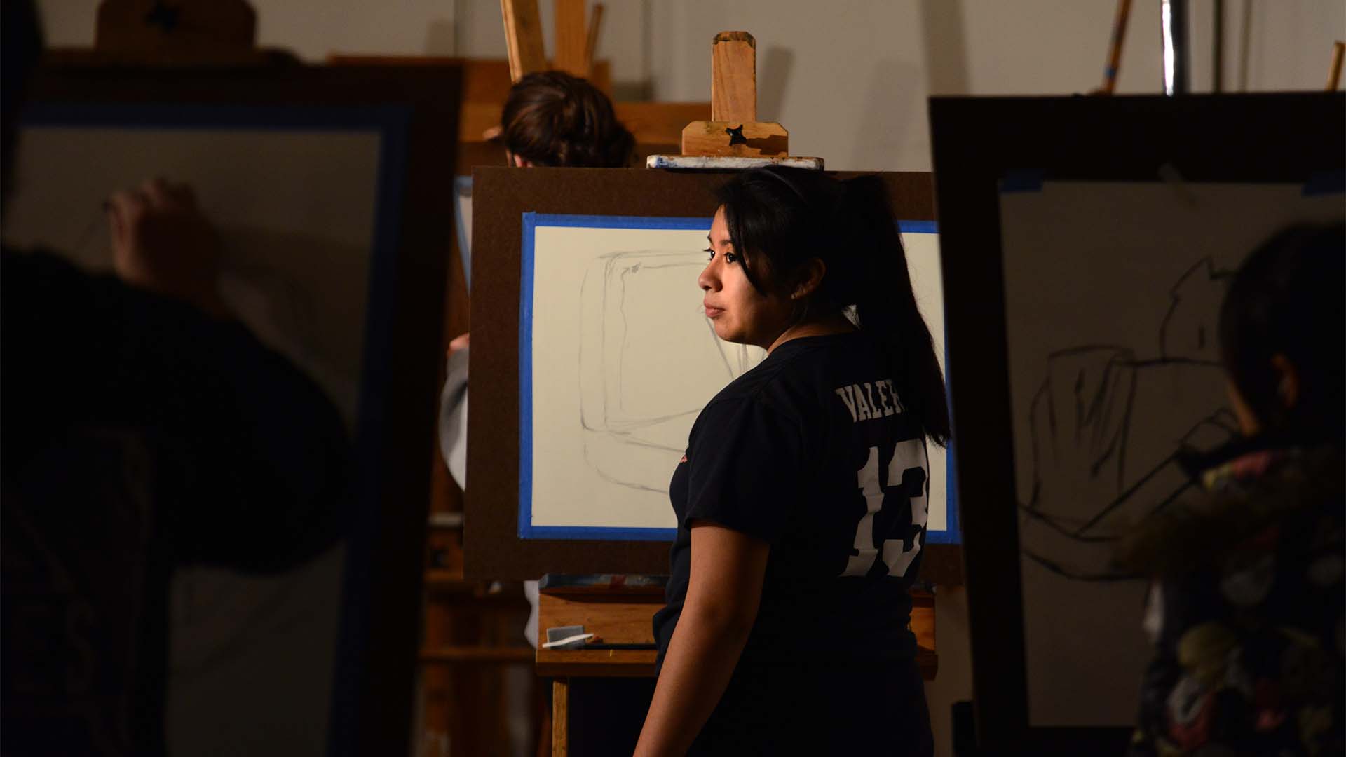 Woman standing with back to camera drawing on an easel with charcoal.