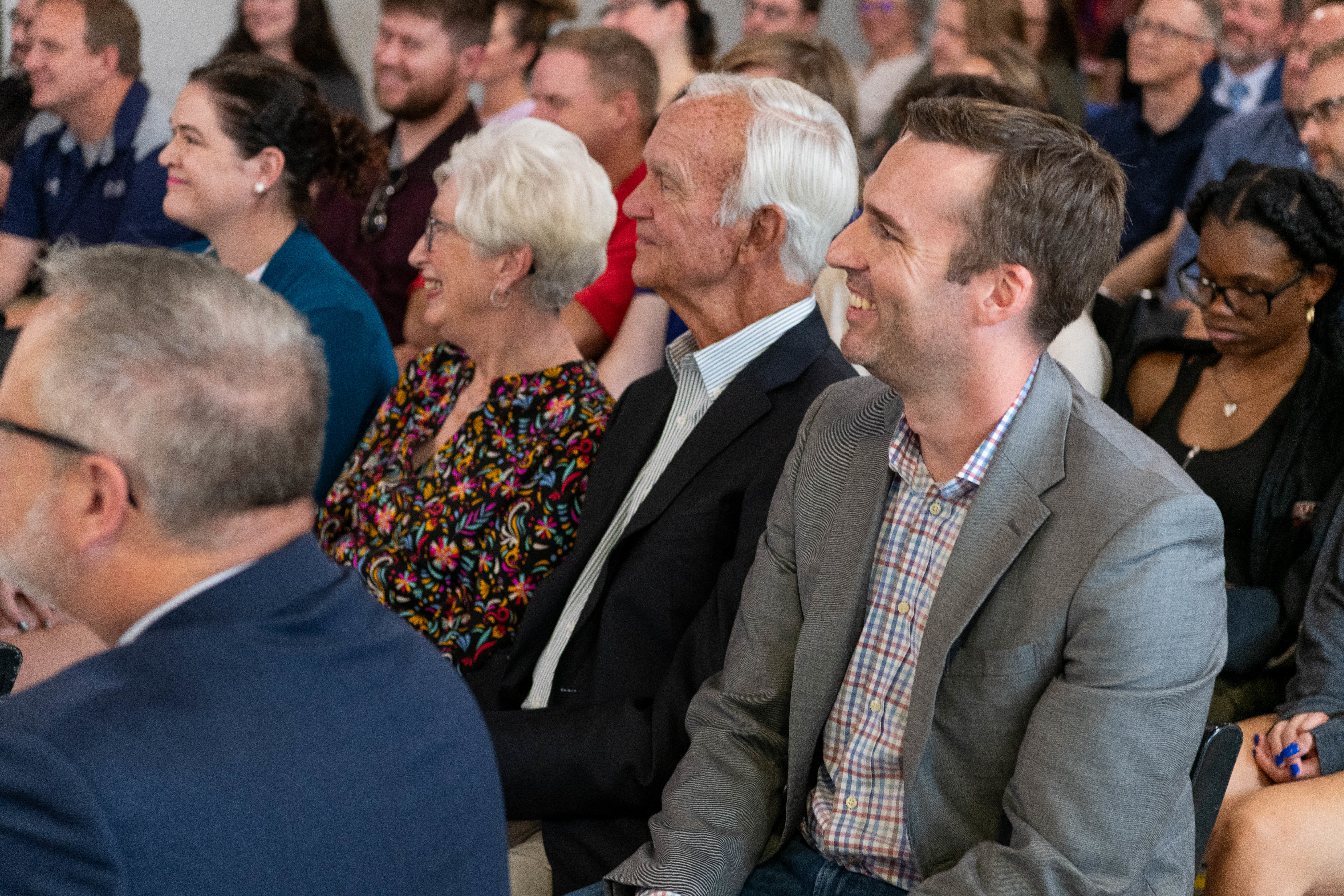 a group of people smiling while sitting in chairs and listening to a presentation