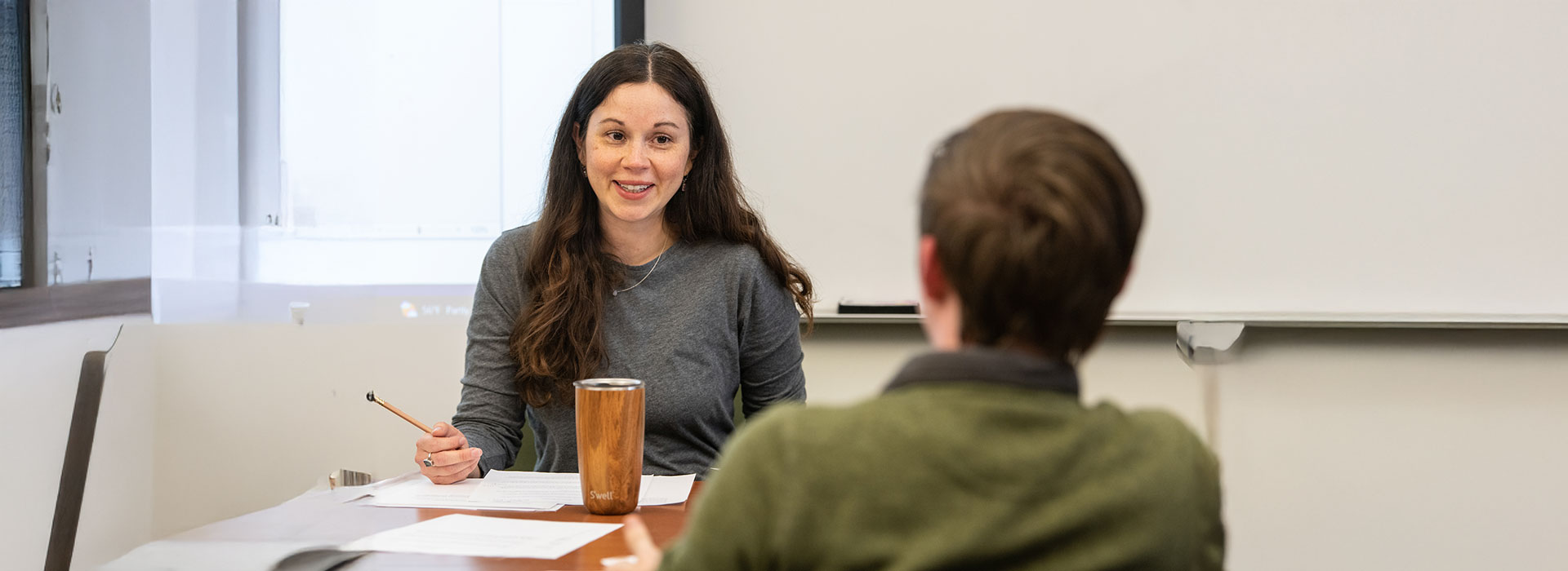 female faculty sitting at a desk, talking to student smiling