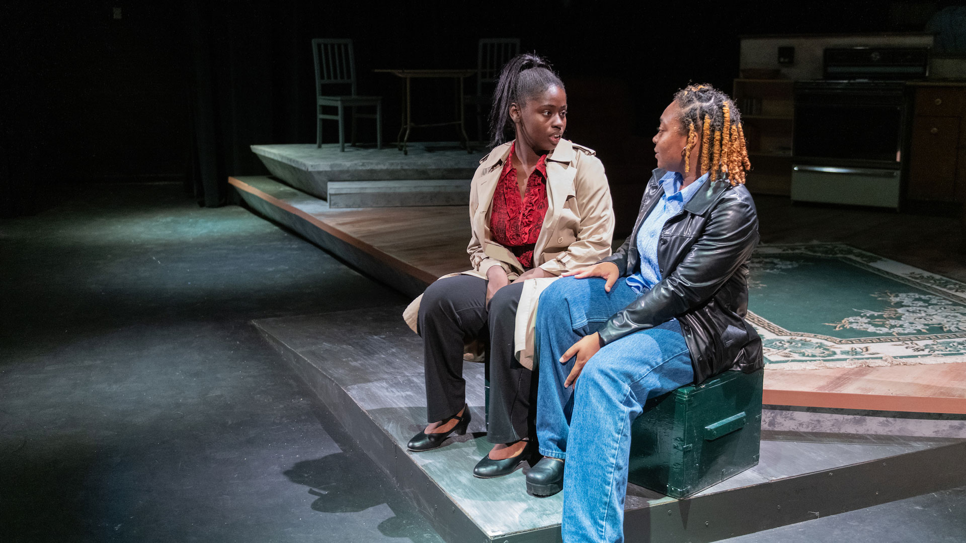 two people sitting on stage in a play talking to each other