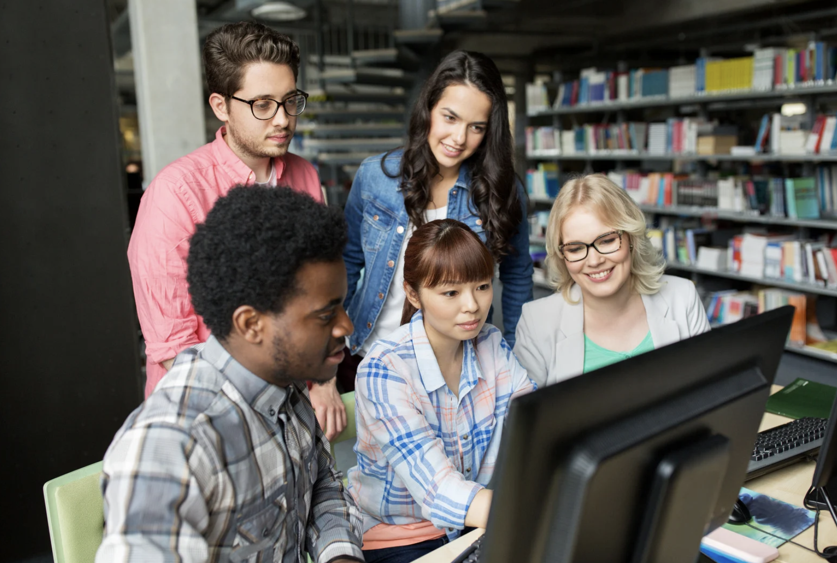 5 members's looking at a computer or a desktop in the library space 