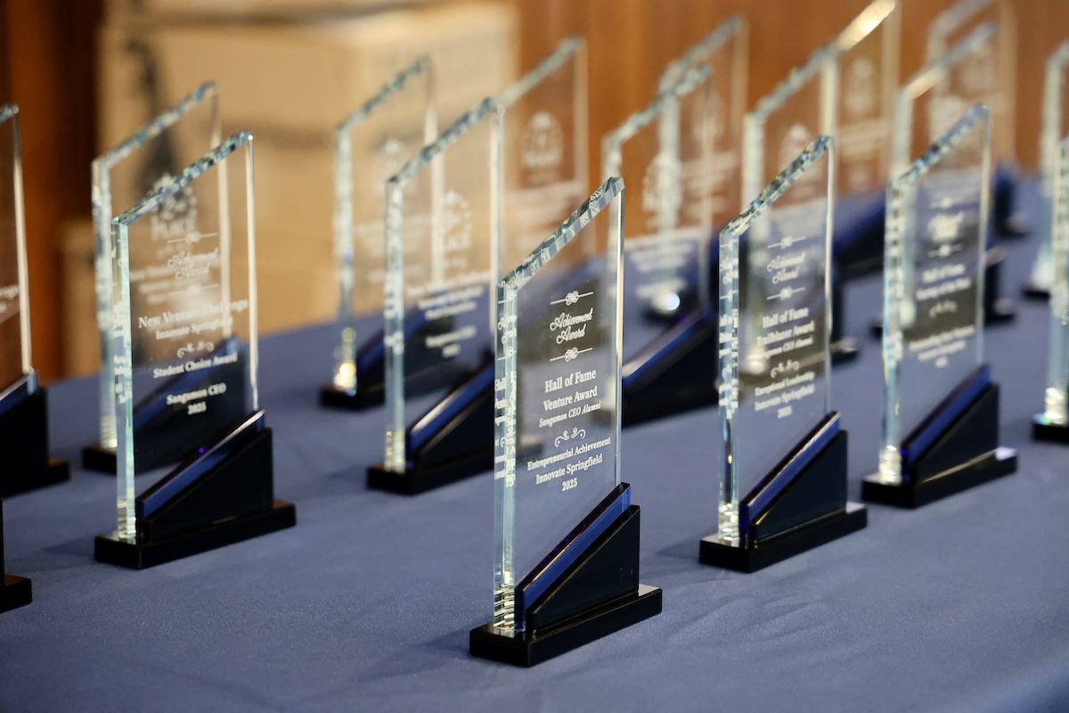 New Venture Challenge glass awards are lined up on a blue tablecloth