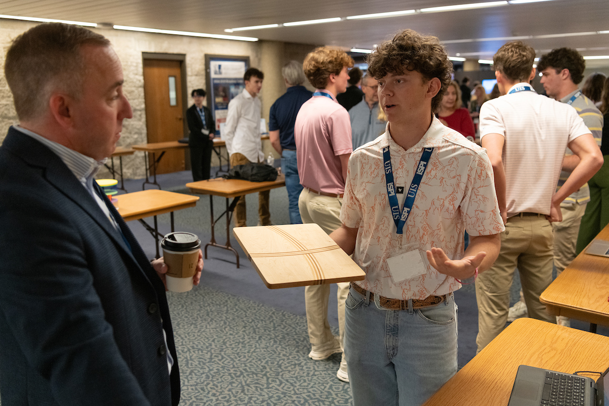 A young man in high school who is a participant of Sangamon CEO discusses their work with an older man with other groups behind them sharing their work.