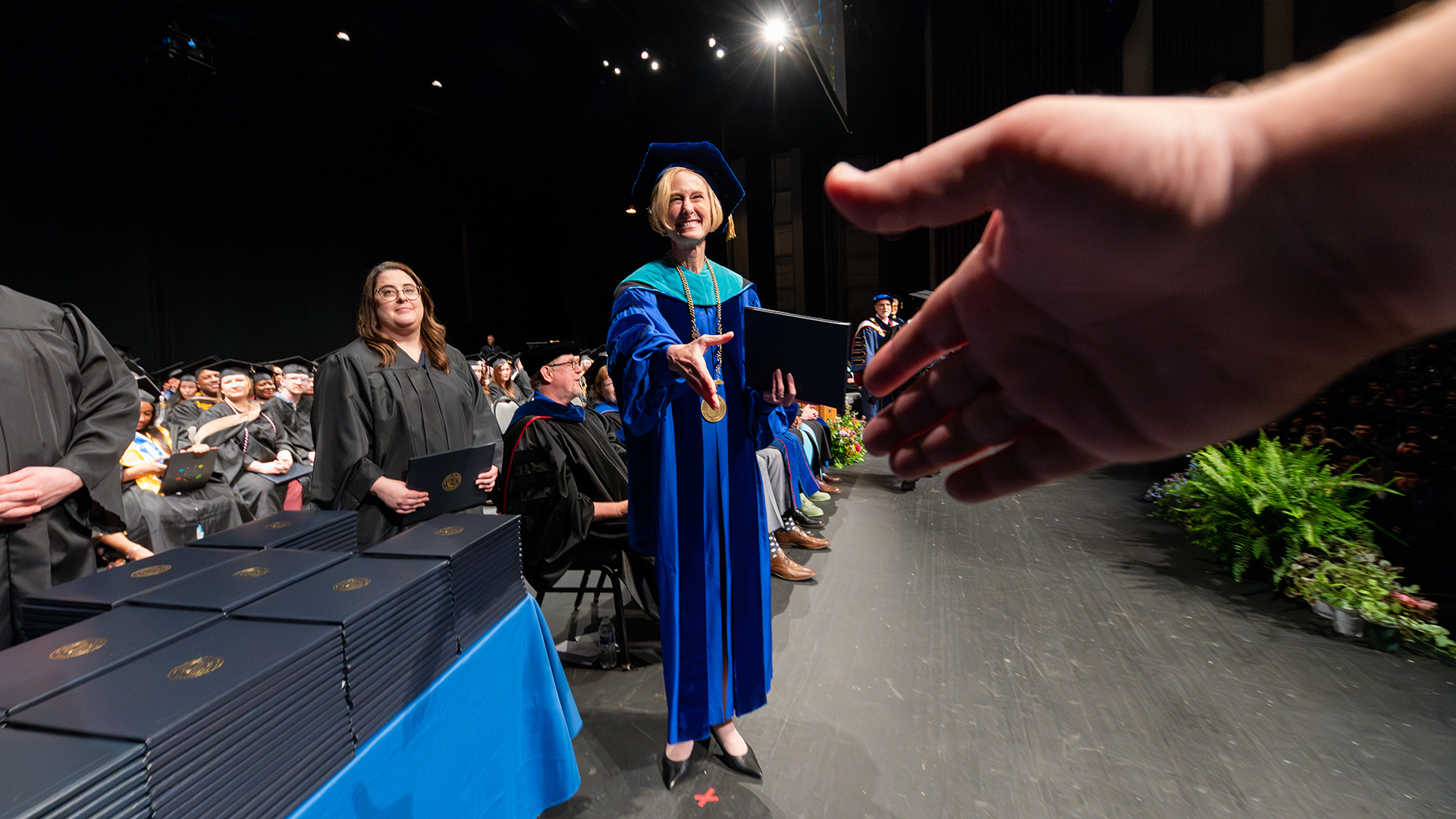First-person perspective of student shaking the Chancellor's hand on the commencement stage.