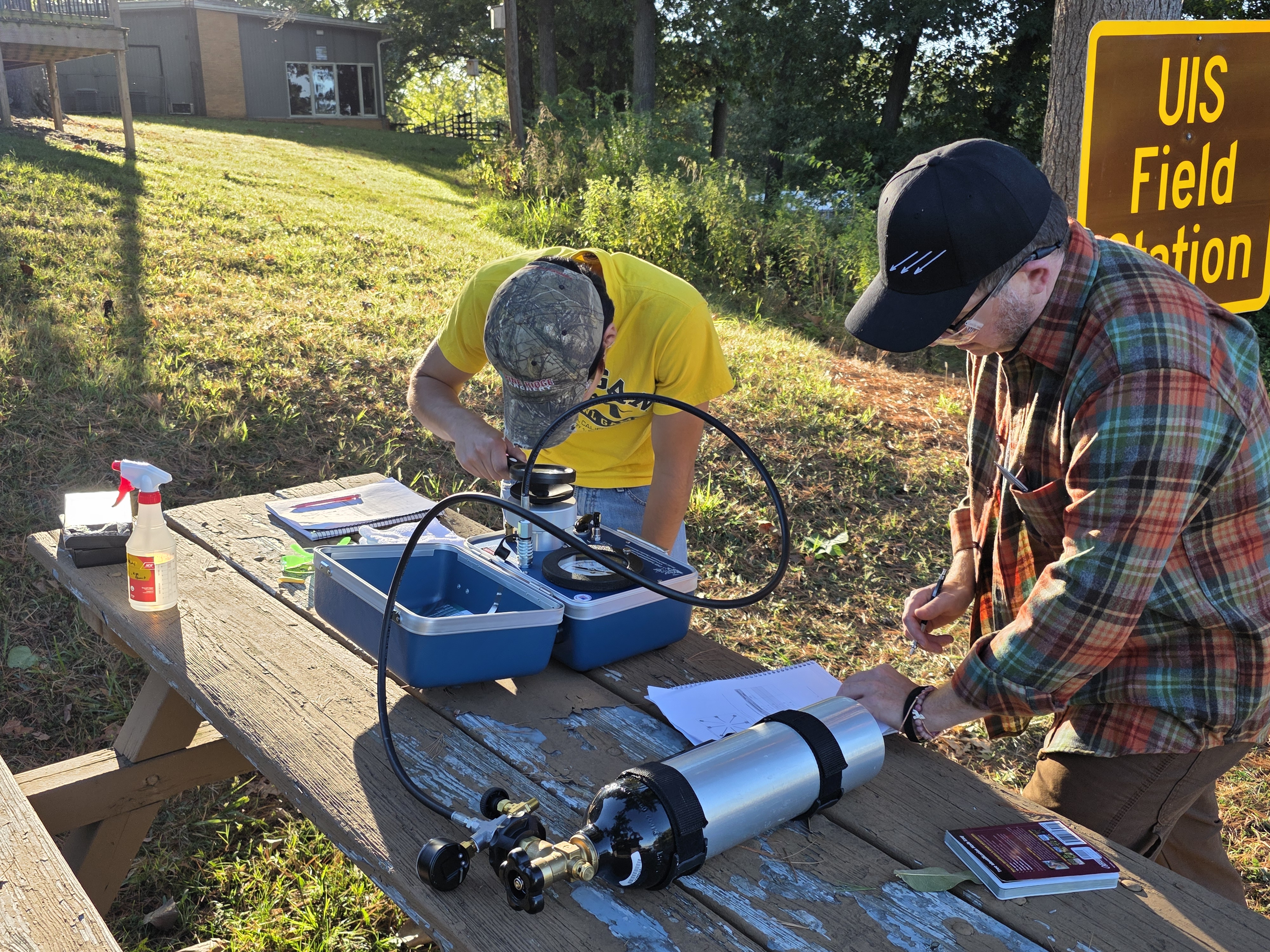 Two researchers calibrating field instruments on a table near the UIS Field Station