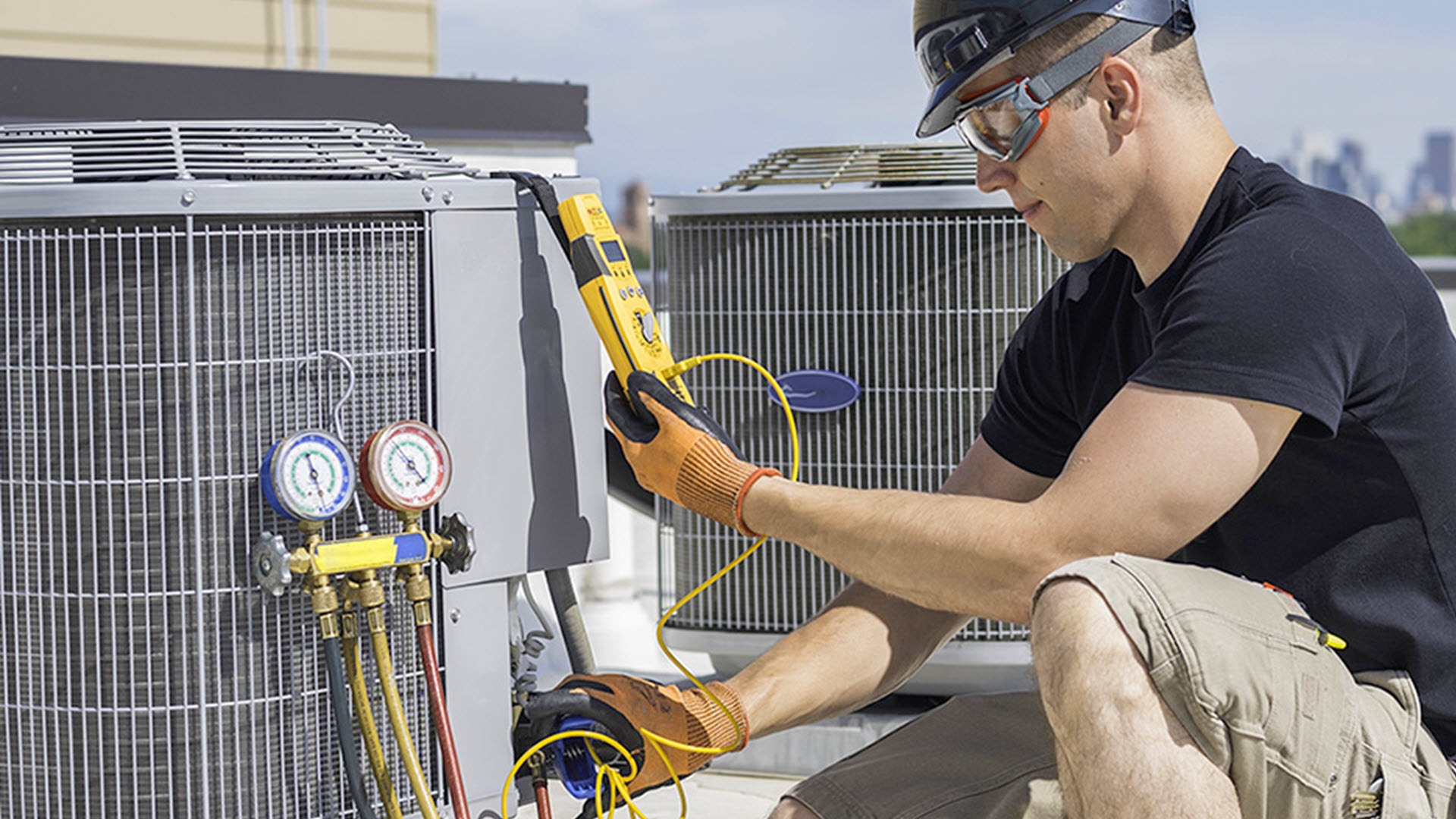Technician checking HVAC unit on rooftop with tools and gauges.