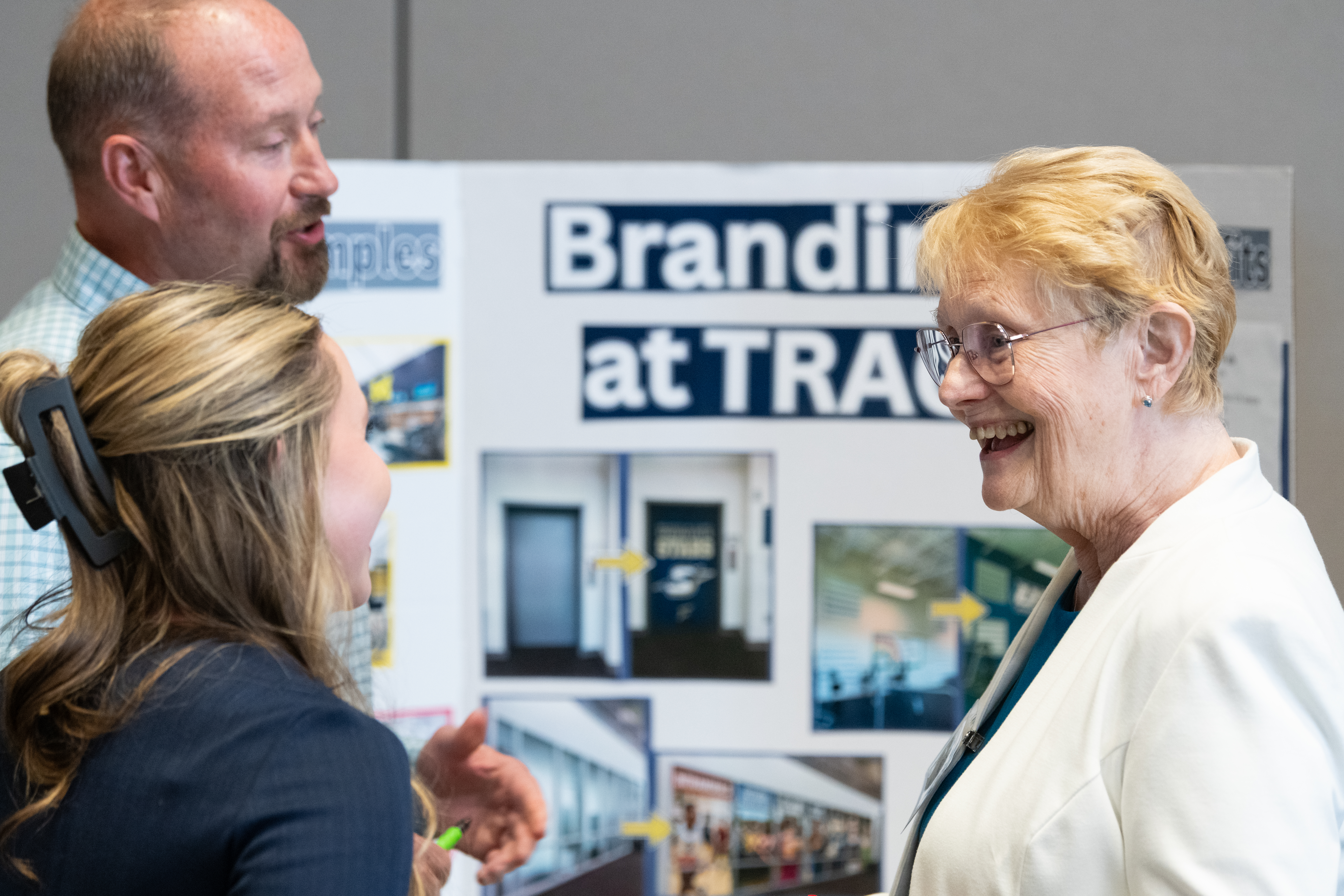 Three people smiling and talking near a branding display board.