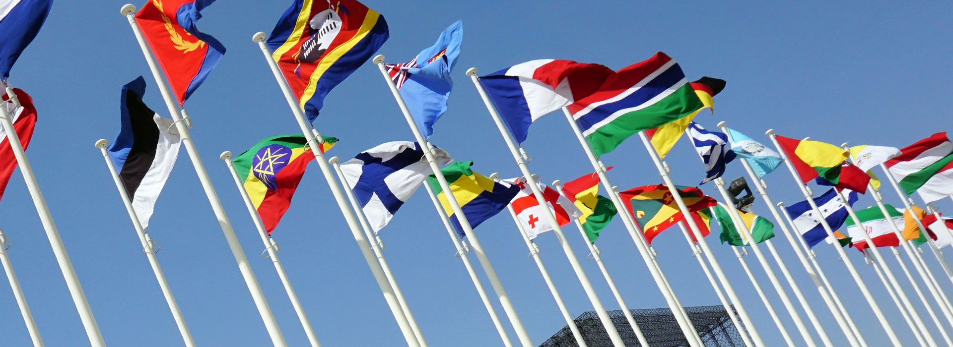 Flags of various countries waving against a clear blue sky.