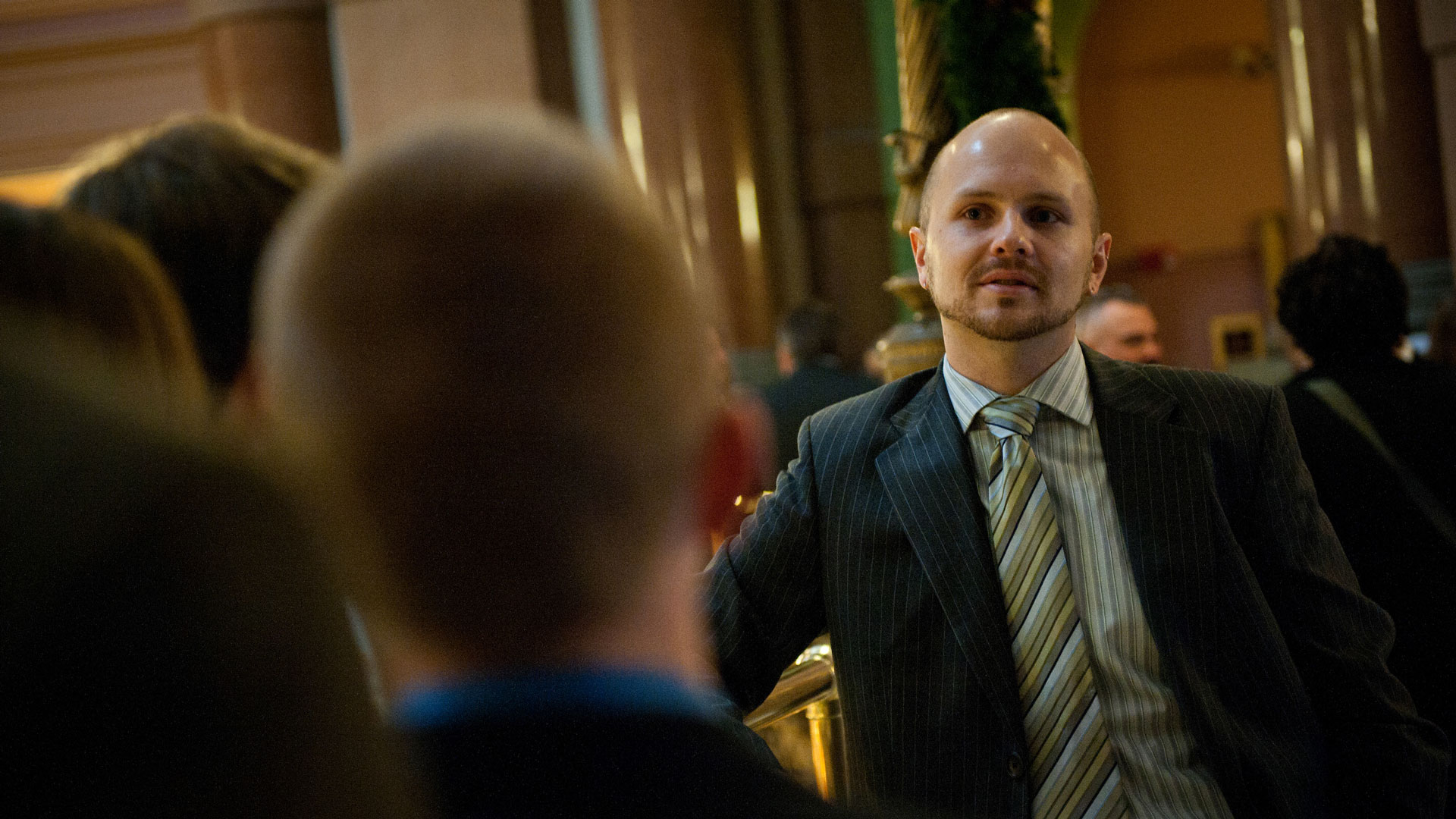 a man in a suit talking to others in a crowded business hall