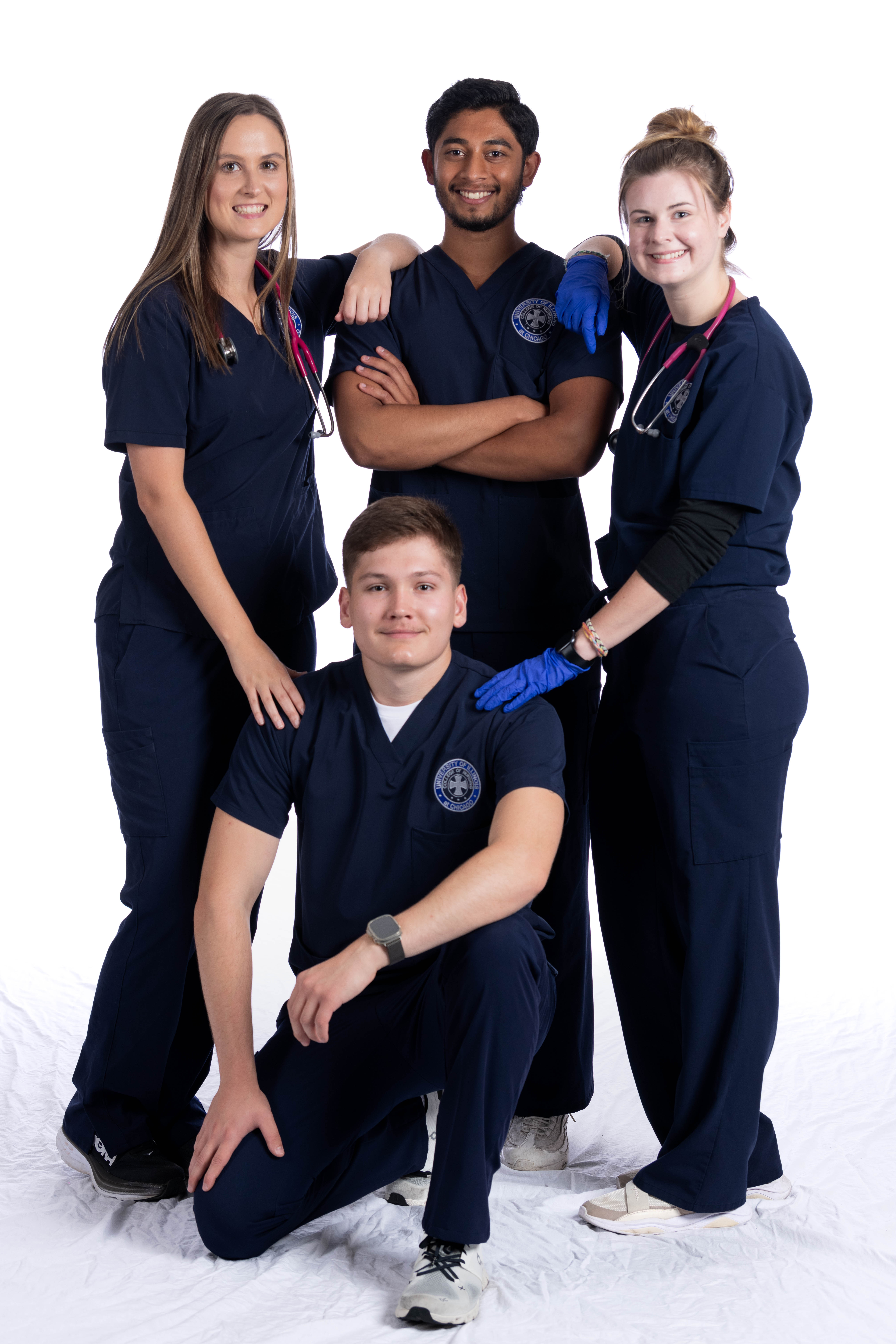 Four nursing students in blue scrubs pose for the camera in front of a white background.