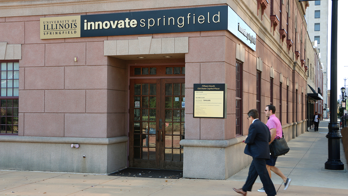 A sign on a building reads Innovate Springfield University of Illinois Springfield as two people walk past