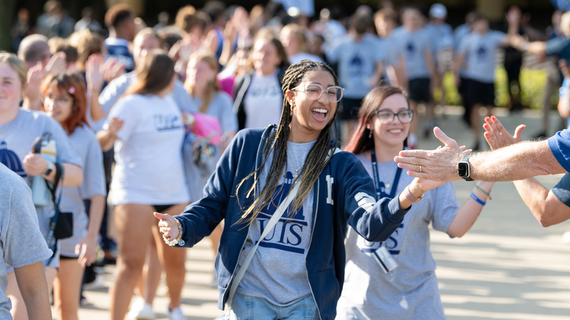 Two students smile while slapping the extended hands of faculty and staff at Convocation.