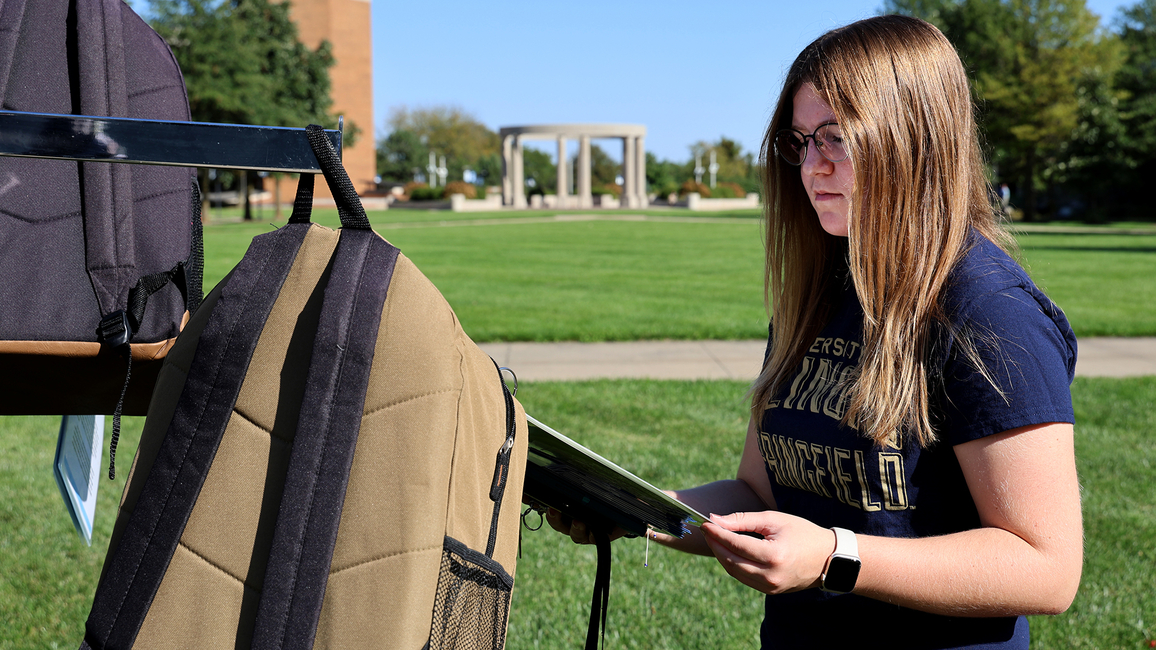 A student reads a story about suicide attached to a backpack on the quad.