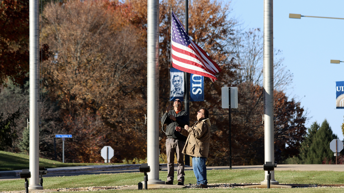 Two veterans raise a flag up a pole.