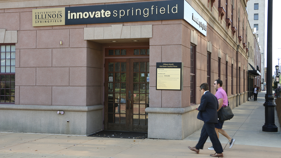 Two people walk in front of a building with a sign reading Innovate Springfield University of Illinois Springfield