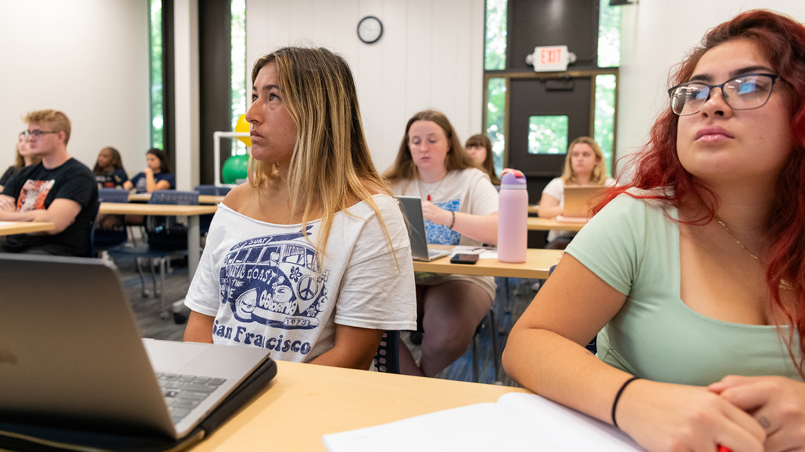 Students attentively listen in a classroom, taking notes and using laptops during a lecture at the University of Illinois Springfield.