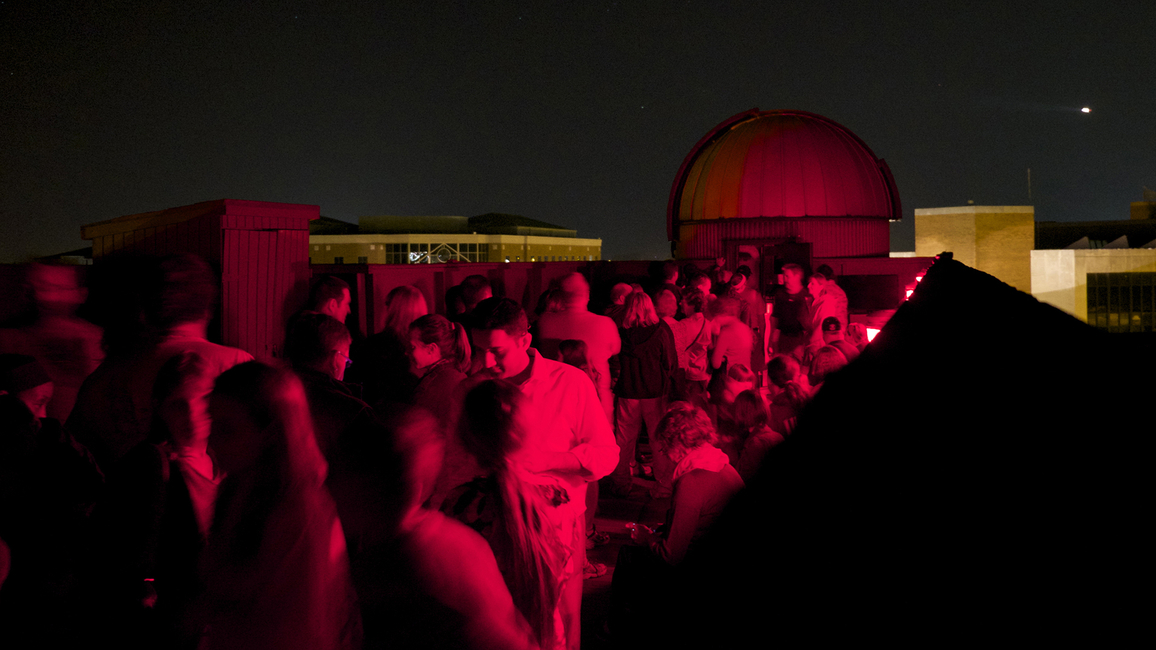 A large group of people on the roof of UIS Brookens Library at night with red lights.