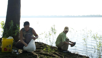 two people cleaning up garbage near a lake