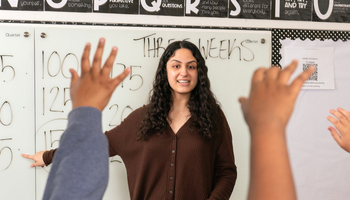 a teacher in the middle of a classroom with lots of raised hands