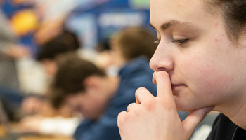 a student at their desk in a classroom looking down at a laptop