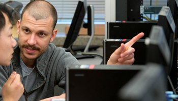 a professor showing a student something on a computer while they sit at a desk