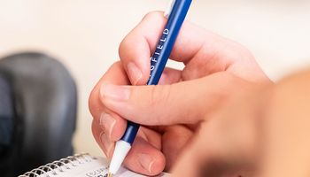 closeup image of a hand writing with a blue UIS pen