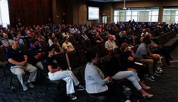 Audience seated in a large conference room, attentively watching a presentation.