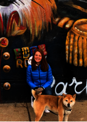 Dr. Magic Wade pictured with her dog in front of a painted mural of a fox on a brick wall