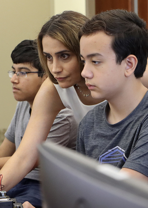 Elham Buxton (center) is shown reaching past a student to control a computer during an AI summer camp.