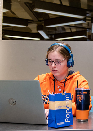 A student wearing headphones uses a laptop computer to study in Brookens Library.