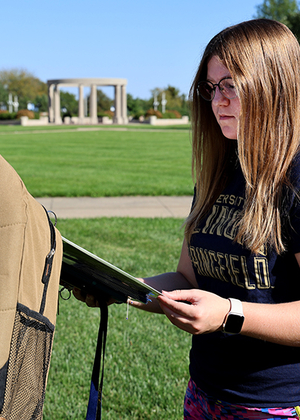 A student reads a story about suicide attached to a backpack on the quad.