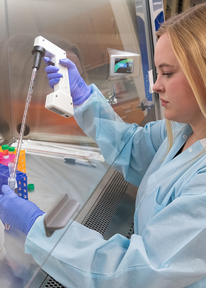 Student in a lab coat and gloves using a pipette for research in a sterile lab environment.