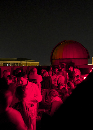 A large group of people on the roof of UIS Brookens Library at night with red lights.