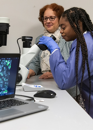Two women in lab coats examining slides under a microscope.