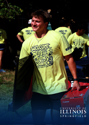 Young man carrying a box, wearing a yellow t-shirt, smiling outdoors.
