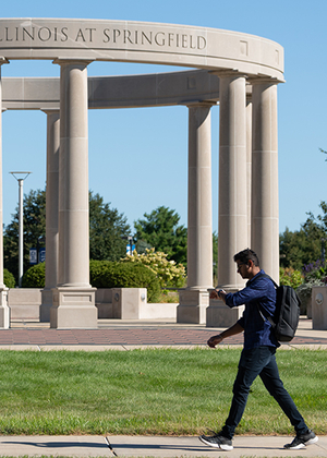 Person walking past a circular column structure with a clear blue sky.