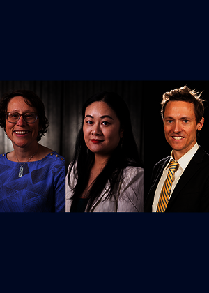 Three people in formal attire, smiling in a dark studio setting.