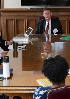 Meeting in a boardroom with people seated around a wooden table.