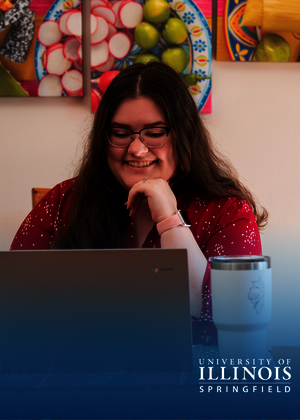 Smiling person with glasses using a laptop, artwork in the background.