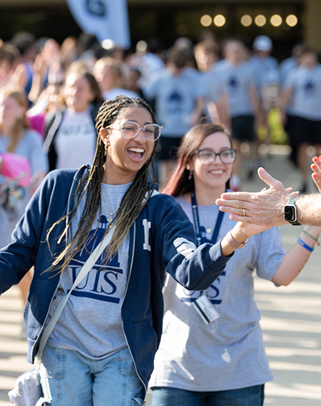 Two students smile while slapping the extended hands of faculty and staff at Convocation.