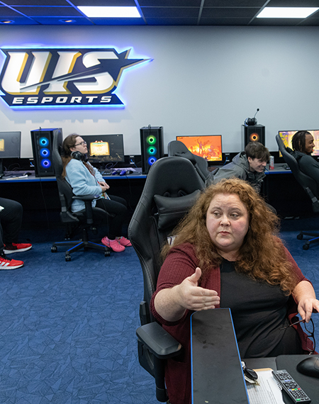 An instructor speaks to students sitting in gaming chairs in the Esports Arena.