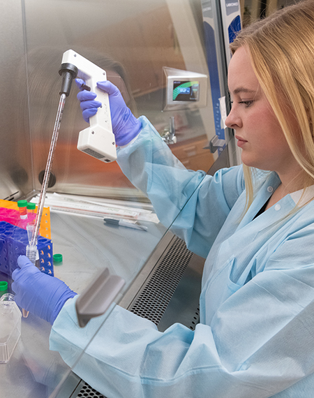 Student in a lab coat and gloves using a pipette for research in a sterile lab environment.