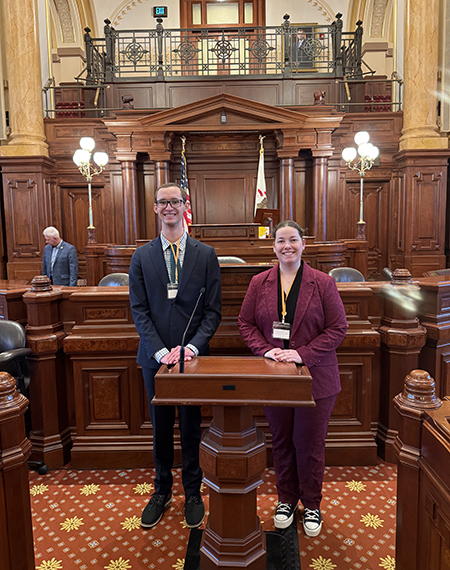 Two students pose on the floor of the Illinois State Senate.