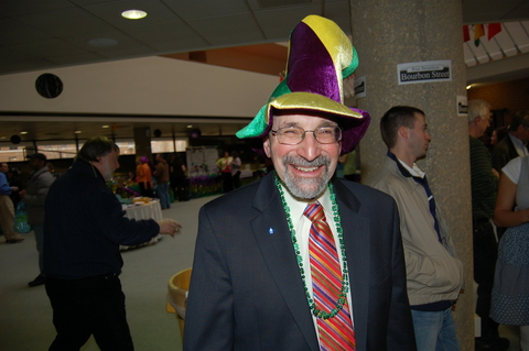 A man smiling who is wearing a Mardi Gras hat.