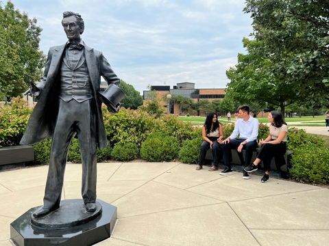 A group of UIS students sitting on a bench talking near a statue of Abraham Lincoln. 
